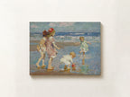 An impressionist-style painting of children playing on a beach, shown as a rectangular canvas mounted on a light beige wall.
