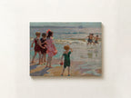 An impressionist oil painting print depicting children playing on a beach, shown hanging on a textured off-white wall.