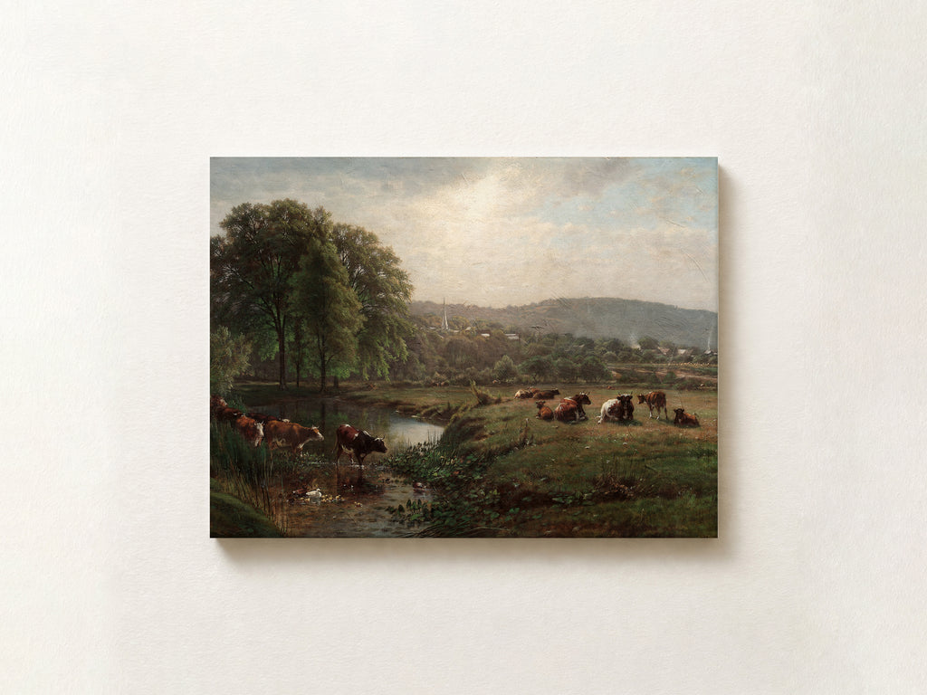A rectangular landscape painting of cows grazing by a river in a green valley, displayed on a light beige wall.