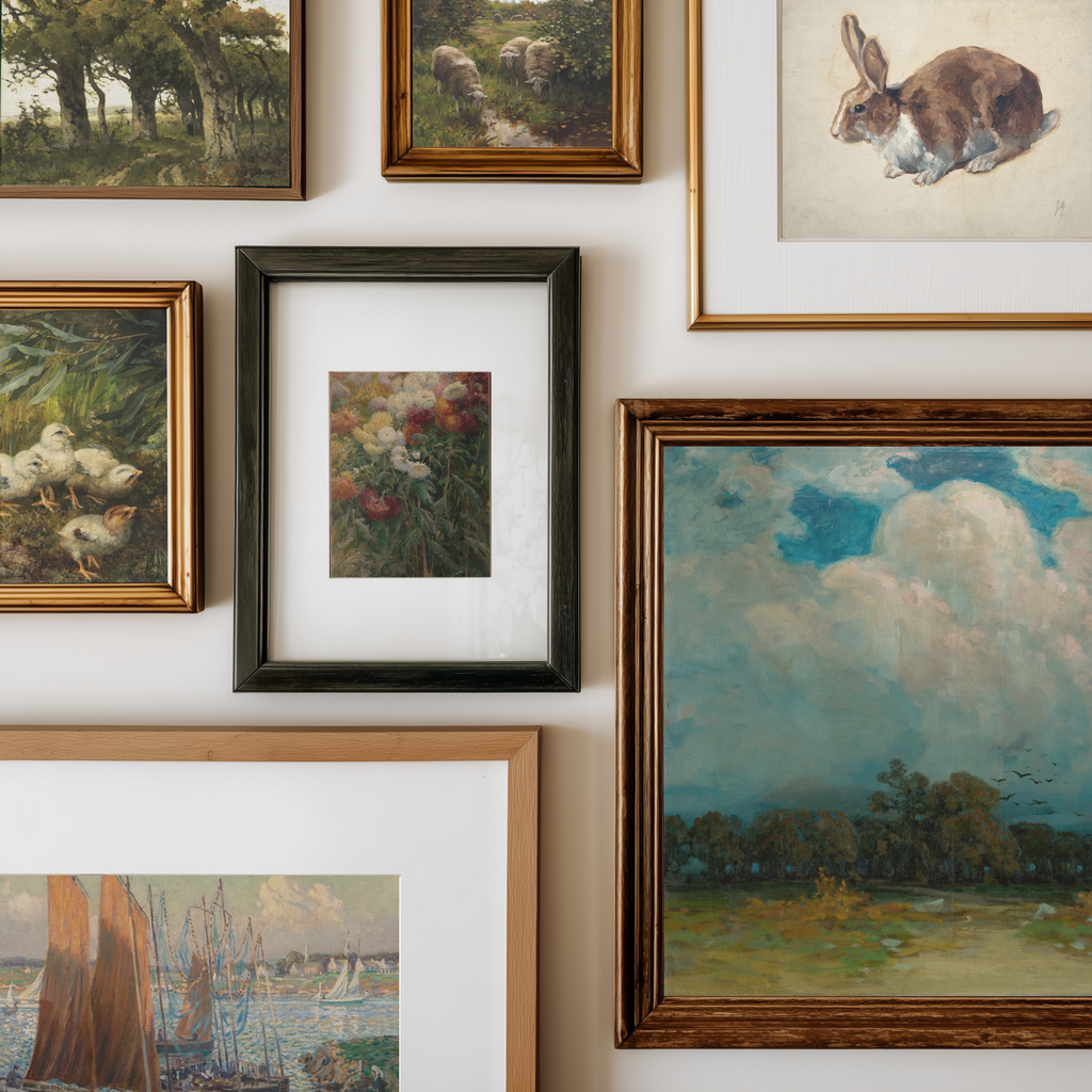 A gallery wall display of multiple framed art prints and paintings, including landscapes, a rabbit study, ducks, flowers, and a seascape, arranged on a white wall.
