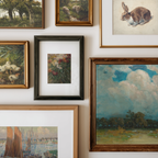 A gallery wall display of multiple framed art prints and paintings, including landscapes, a rabbit study, ducks, flowers, and a seascape, arranged on a white wall.