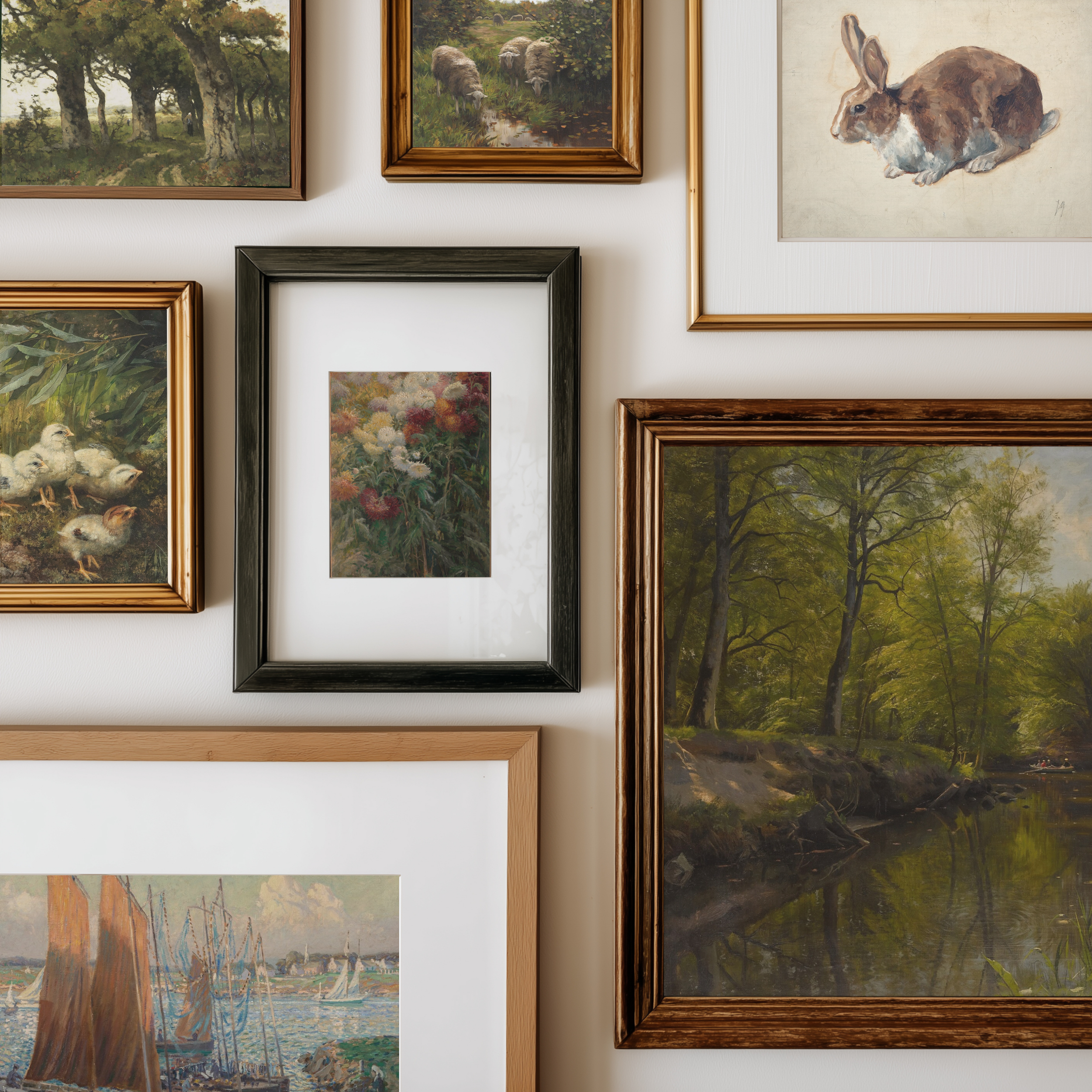 A gallery wall display of multiple framed art prints and paintings, including landscapes, a rabbit illustration, ducks, and flowers, arranged on a light beige wall.