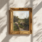 A framed landscape painting of sheep grazing in a grassy field near a stream, displayed on a textured white wall with soft window shadow patterns.