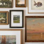 A gallery wall display of multiple framed paintings and art prints in different styles and colors, including landscapes, a rabbit sketch, ducks, and a sunset scene.
