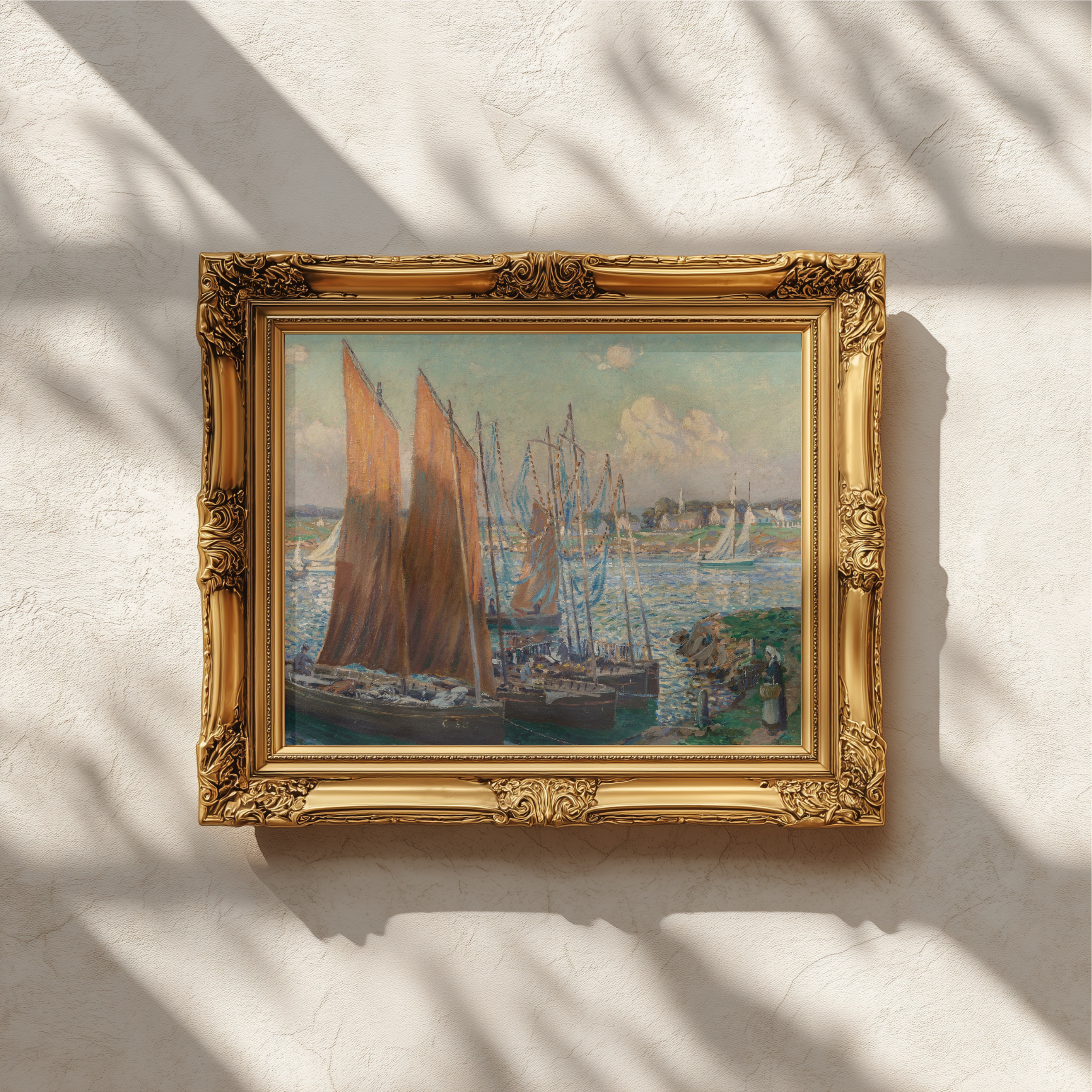 An ornate gold picture frame holding a painting of sailing ships on the water, hung on a textured off-white wall with soft window shadows cast across it.