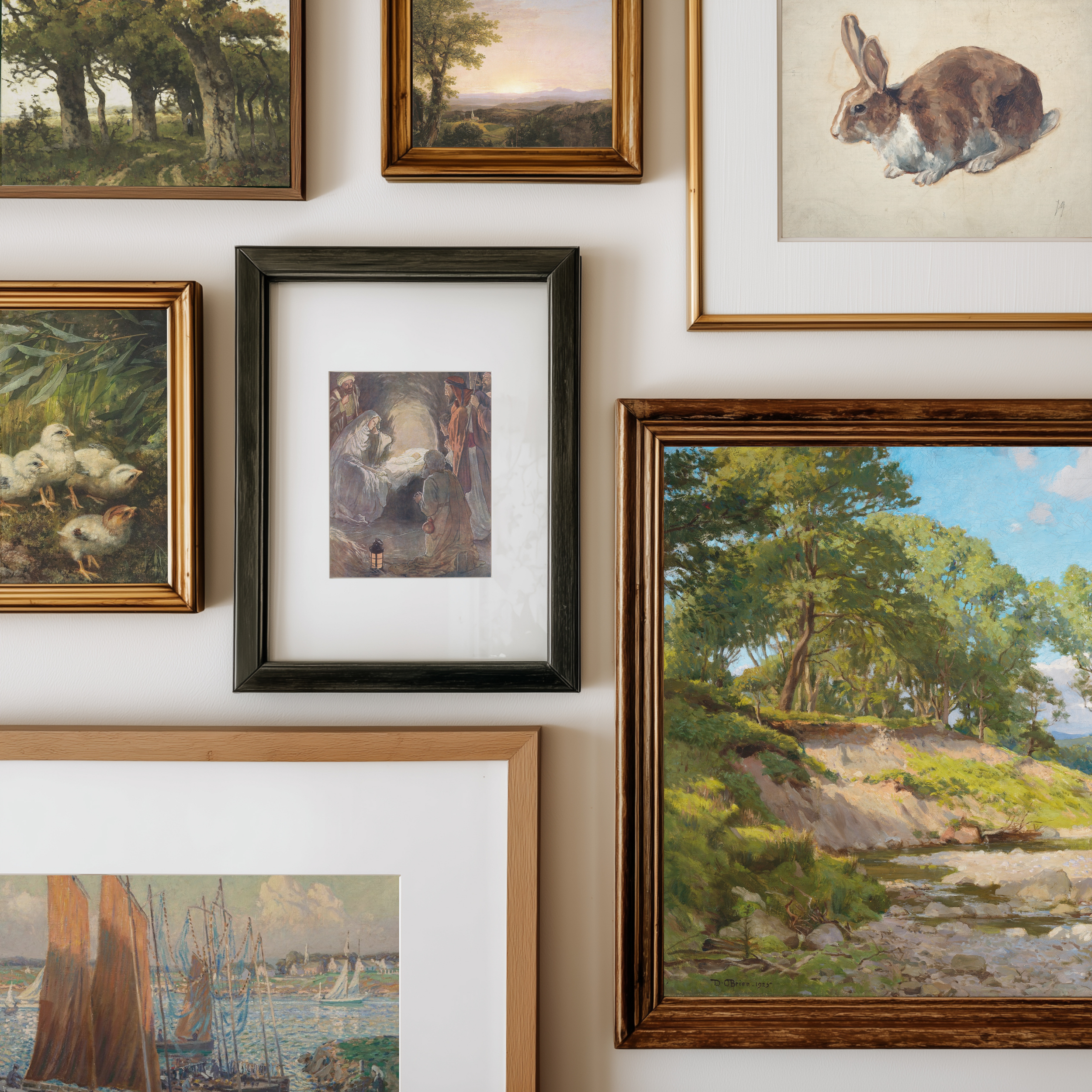 A gallery wall display of multiple framed art prints and paintings, including landscapes, a rabbit illustration, ducks, and a central dark-framed artwork, arranged on a white wall.