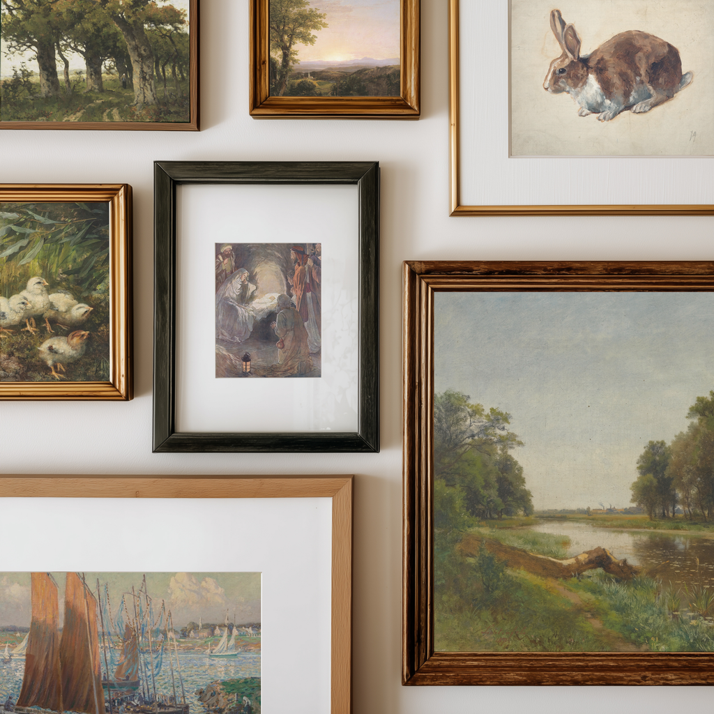 A gallery wall display of multiple framed art prints and paintings, including landscapes, a rabbit study, ducks, and a central dark-framed artwork, arranged on a white wall.