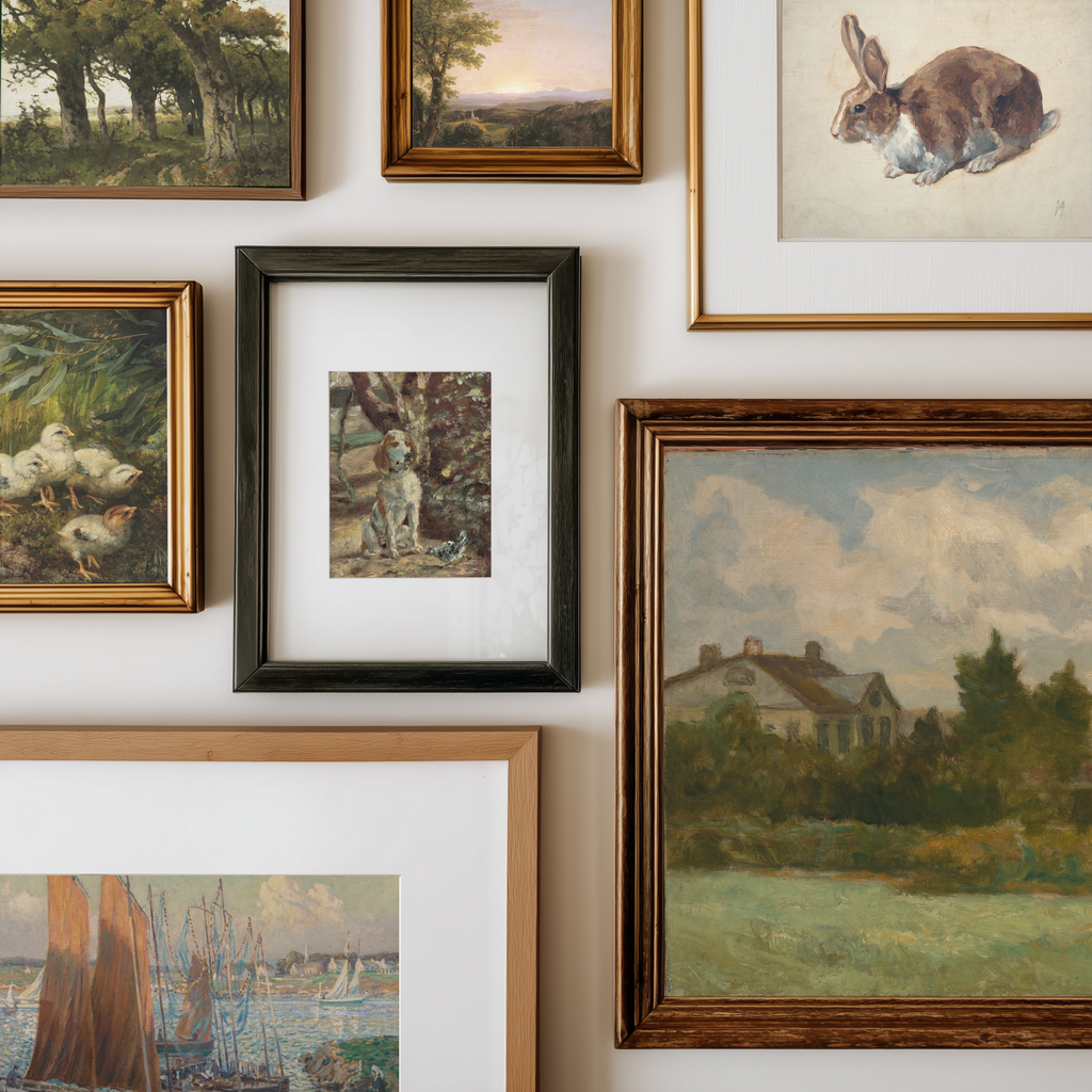 A gallery wall display of multiple framed art prints and paintings, including landscapes, a rabbit portrait, ducks, a dog, and a house scene, arranged on a white wall.