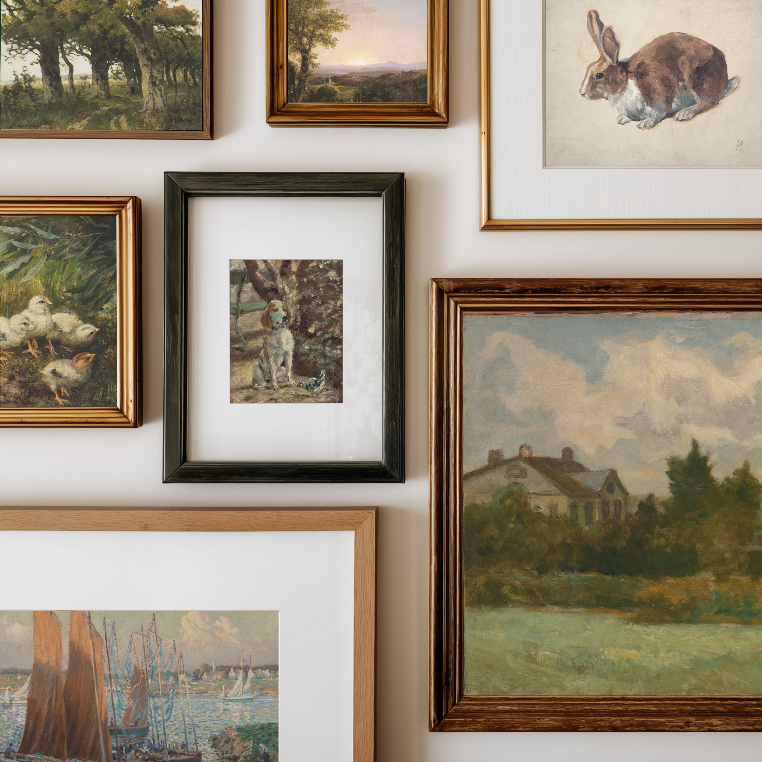 A gallery wall display of multiple framed art prints and paintings, including landscapes, a rabbit portrait, ducks, a dog, and a house scene, arranged on a white wall.