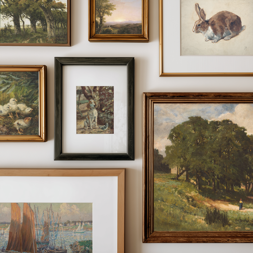 A gallery wall display of multiple framed art prints and paintings, including landscapes, a rabbit portrait, ducks, a dog, and a harbor scene, arranged on a light neutral wall.