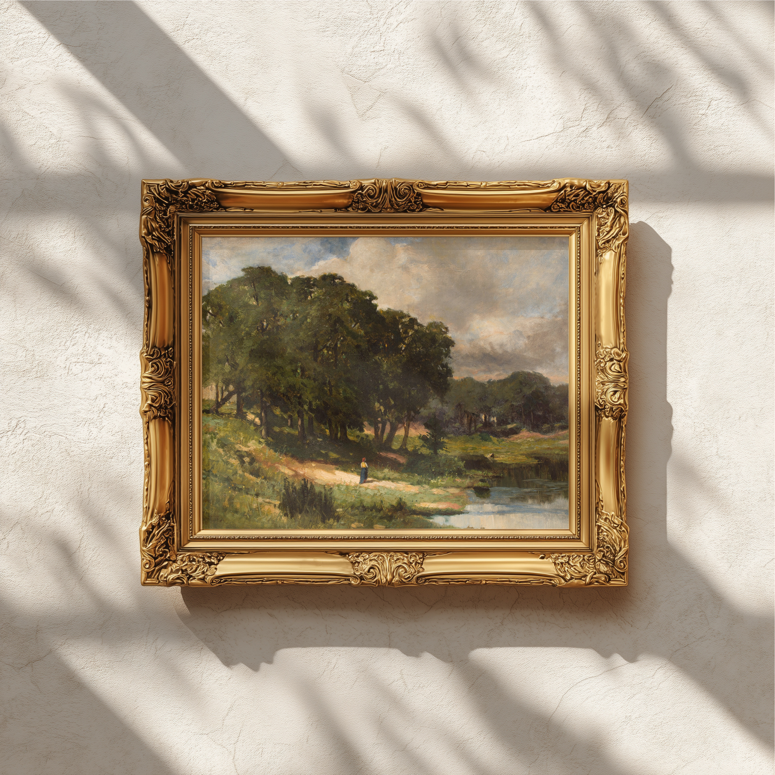 An ornate gold-framed landscape painting hanging on a textured white wall, with soft shadows cast across the scene.