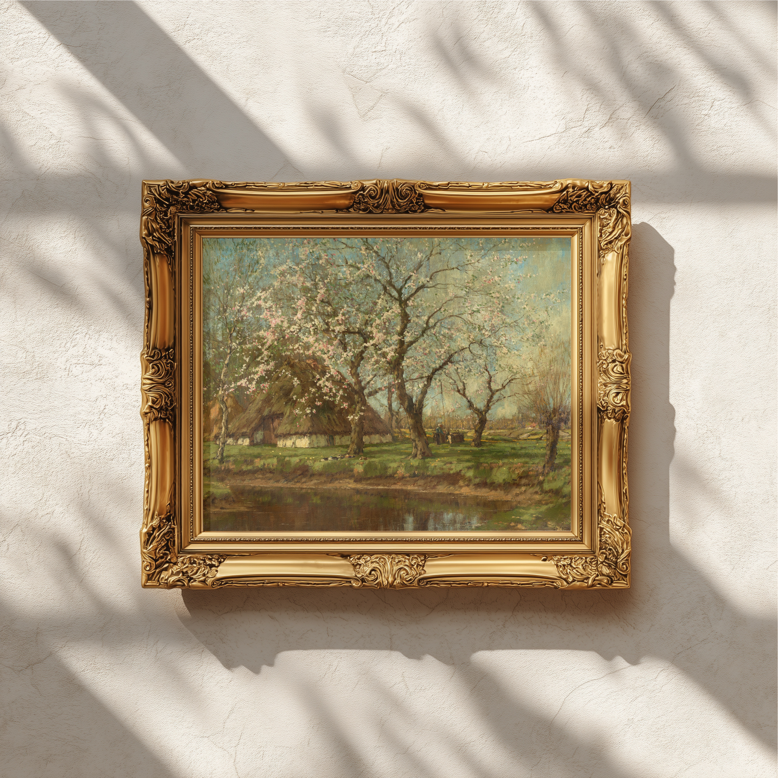 An ornate gold picture frame containing a landscape painting of blooming trees, mounted on a textured white wall with soft window shadow patterns.