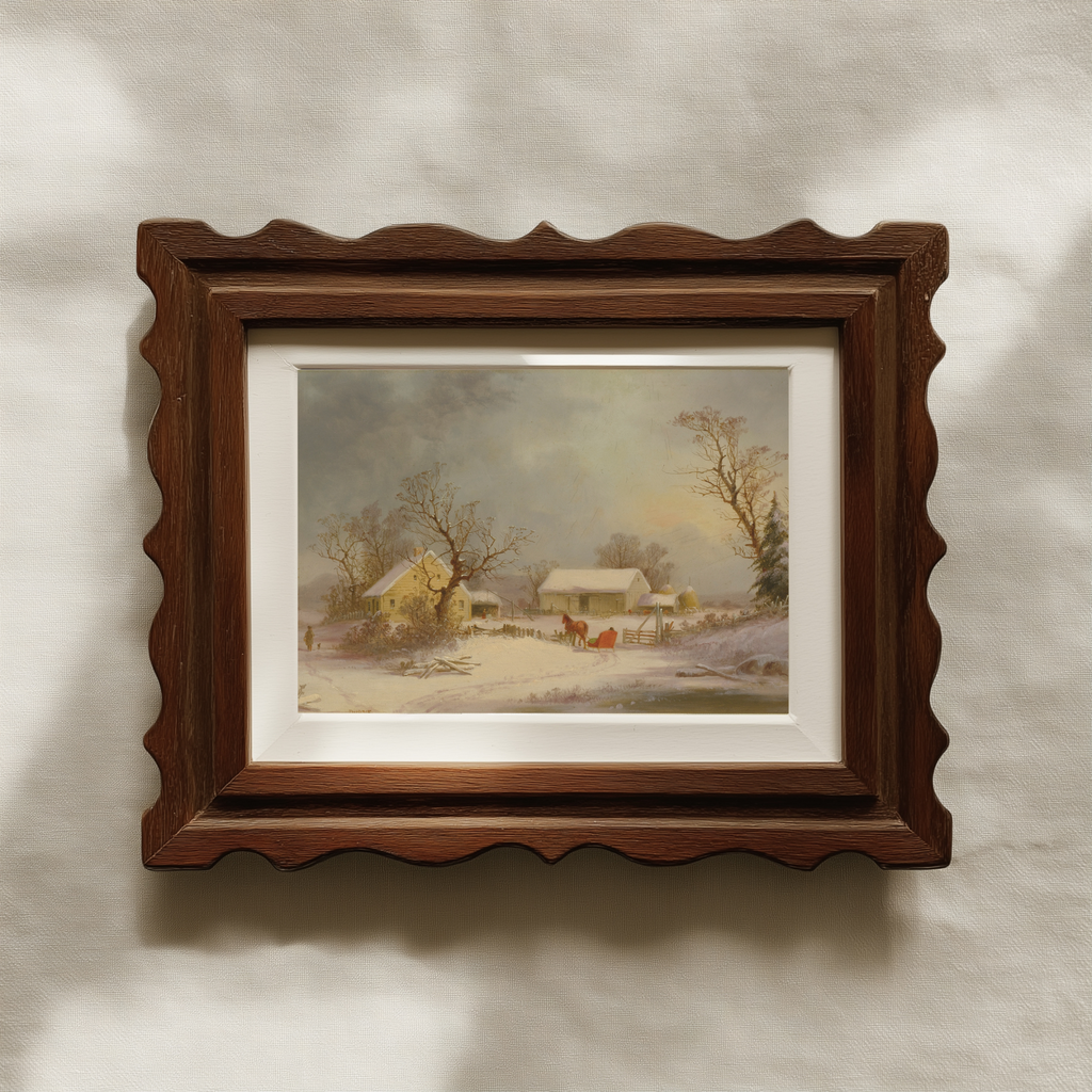 A framed landscape art print featuring a snowy village scene, housed in a dark brown wooden frame with a decorative scalloped edge and a white mat, mounted on a textured beige wall.