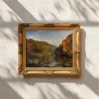 An ornate gold picture frame holding a landscape painting of a waterfall and autumn trees, mounted on a textured white wall with soft leaf shadows cast across it.