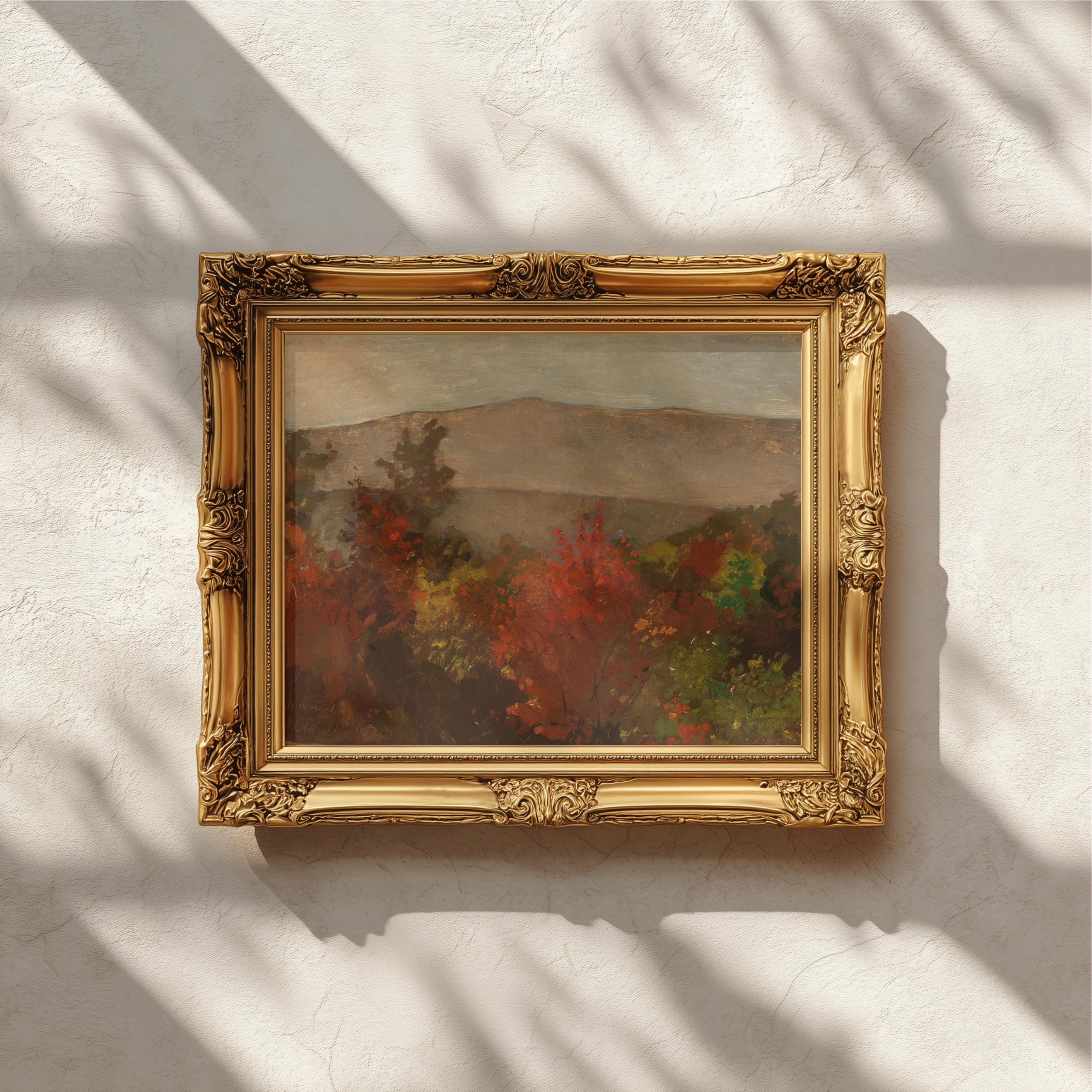 An ornate gold picture frame holding an impressionistic painting with red, green, and gray tones, mounted on a textured off-white wall with soft leaf shadows cast across it.