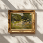 An ornate gold-framed painting of a lush green landscape hangs on a textured white wall, with soft shadows cast across the scene.