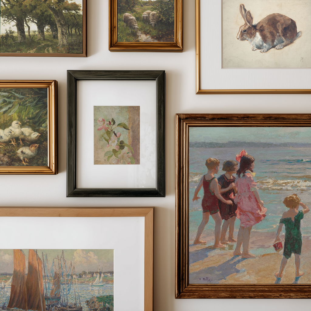 A gallery wall display of multiple framed art prints and paintings in various frames, including a rabbit illustration, a beach scene with children, ducks, trees, and a small floral painting.
