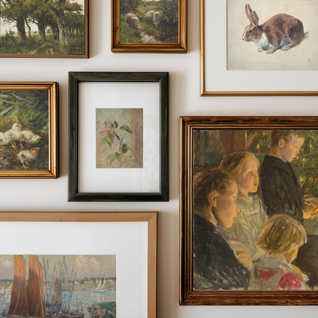 A gallery wall display of multiple framed art prints and paintings in various frames, including landscapes, portraits, and still life scenes, arranged on a white wall.