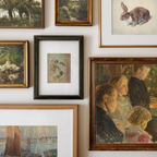 A gallery wall display of multiple framed art prints and paintings in various frames, including landscapes, portraits, and still life scenes, arranged on a white wall.