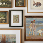 A gallery wall display of multiple framed art prints and paintings in various frames, including landscapes, portraits, and still life scenes, arranged on a light-colored wall.
