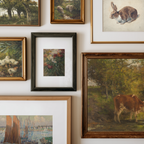 A gallery wall display of multiple framed art prints and paintings, including landscapes, animals, and floral subjects in various frame styles against a white wall.