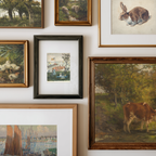 A gallery wall display of multiple framed art prints and paintings in various frames, including landscapes, animals, and a small village scene.