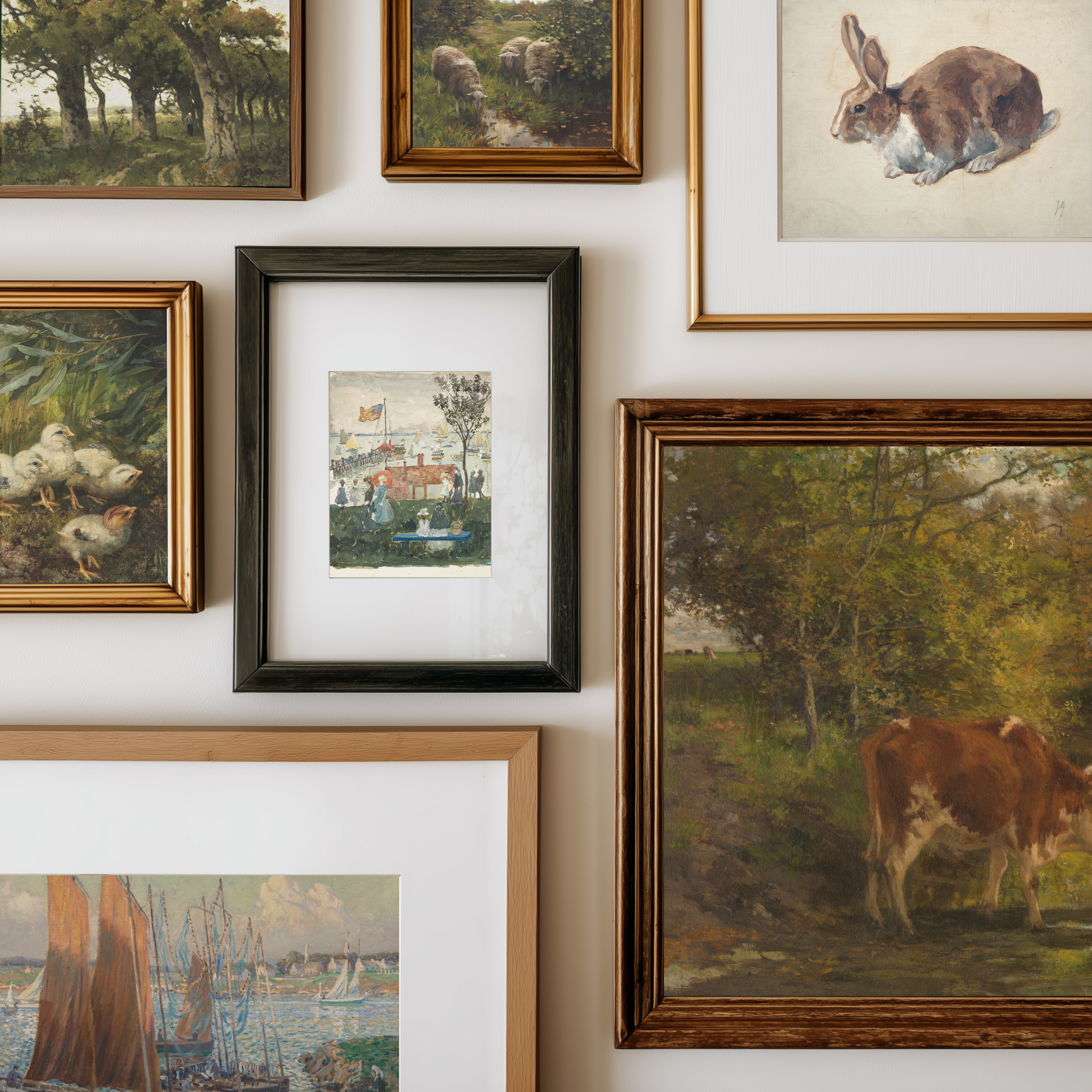 A gallery wall display of multiple framed art prints and paintings in various frames, including landscapes, animals, and a small village scene.
