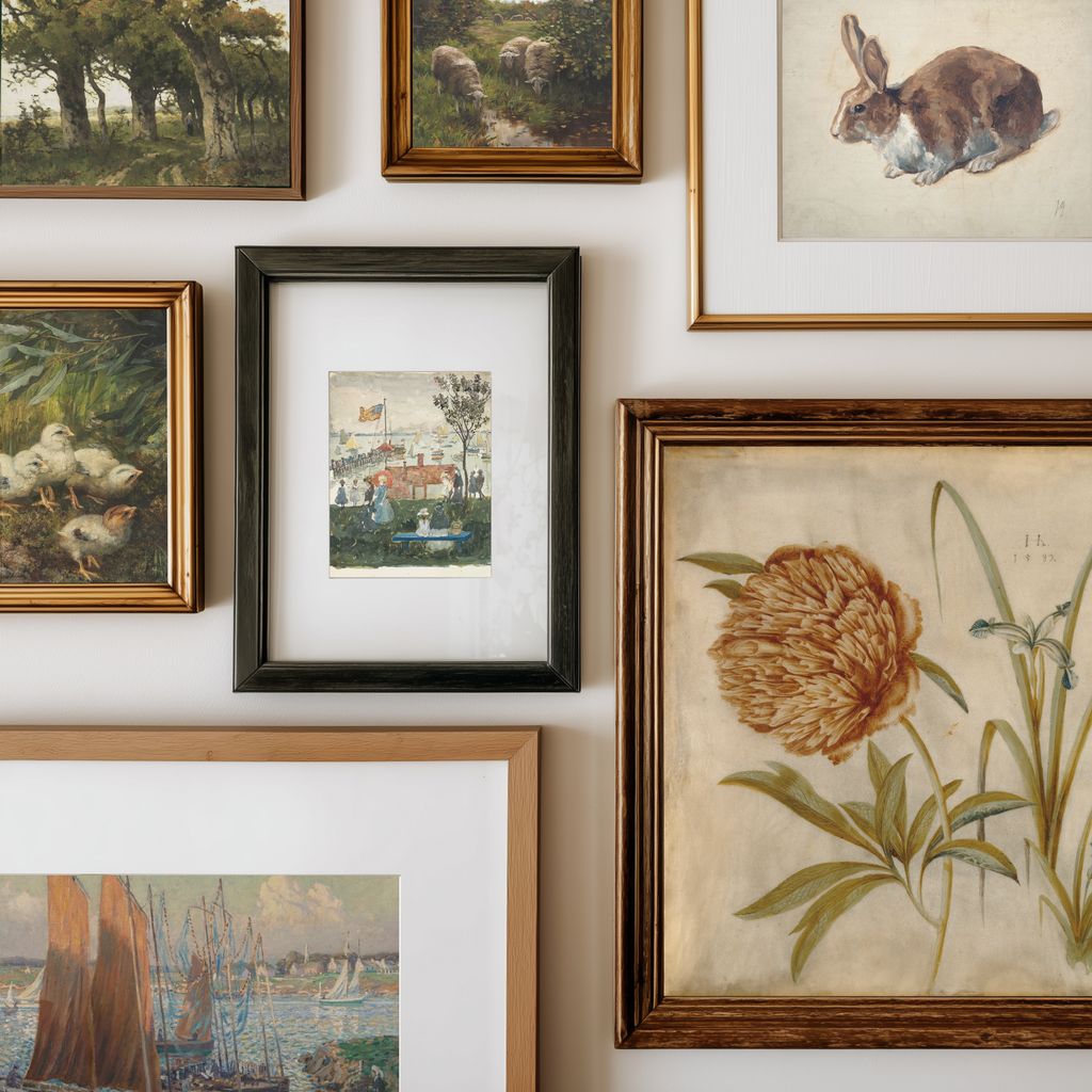 A gallery wall display of multiple framed art prints and paintings, including a rabbit, a duck, a landscape, a small village scene, and a botanical flower print, each in different frame styles against a white wall.