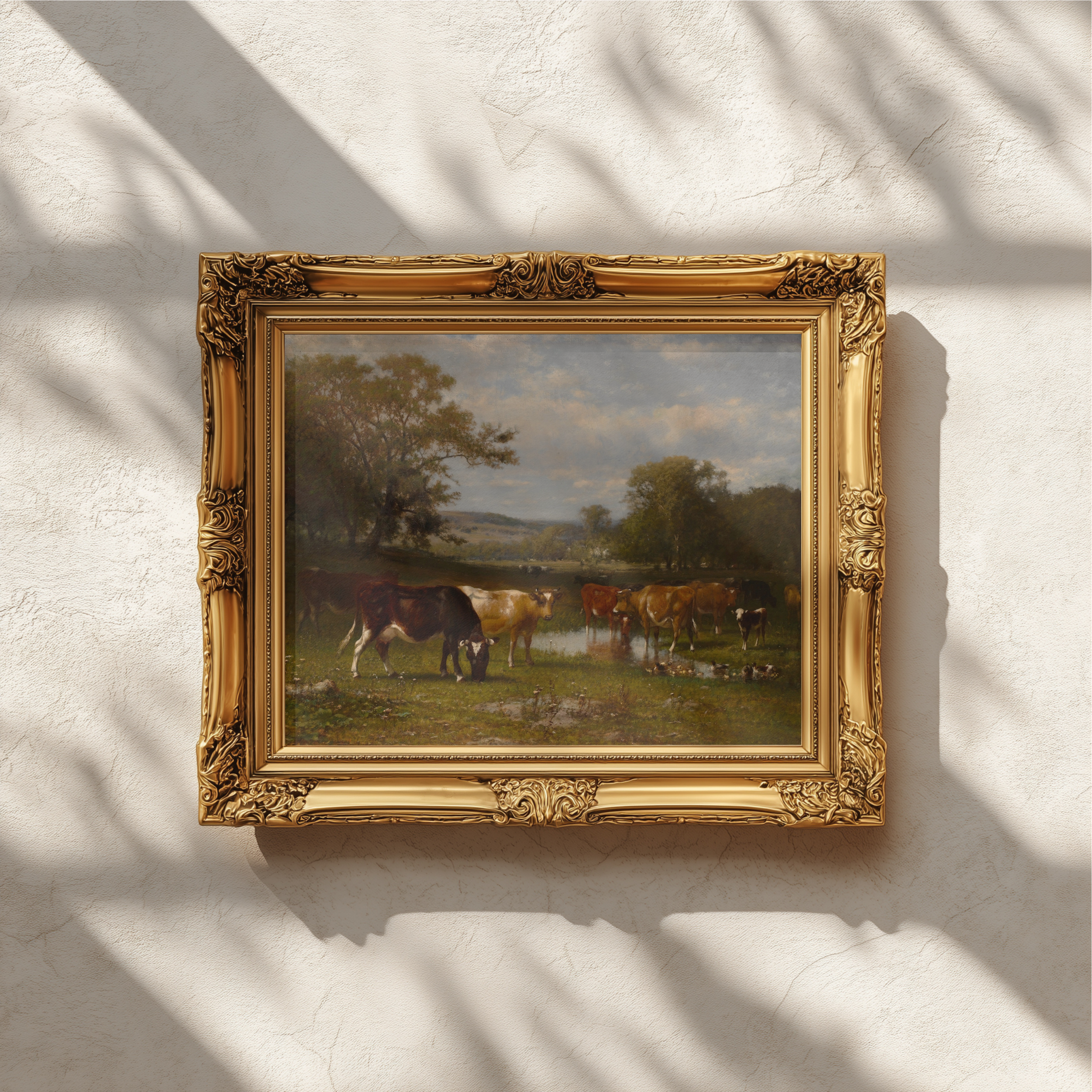 An ornate gold picture frame holding a landscape painting of horses by a river, mounted on a textured white wall with soft shadow patterns.