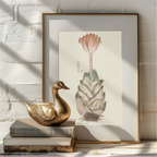 A framed botanical art print featuring a succulent and flower, styled on a white brick wall next to a gold duck figurine on stacked books.