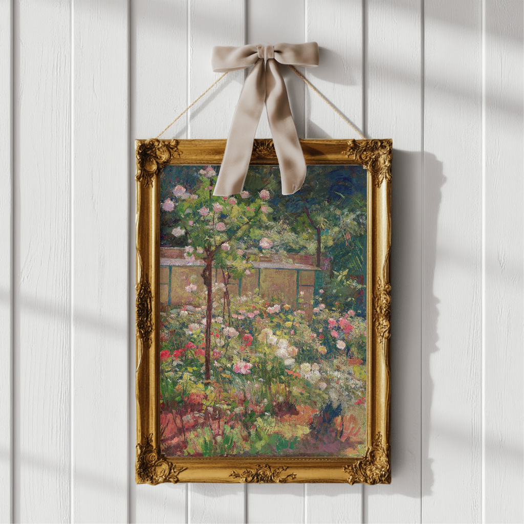 A framed floral landscape painting hangs on a white paneled wall with a beige ribbon bow at the top. The ornate gold frame contains a colorful painting of a garden with pink, white, and green flowers, and a house in the background.