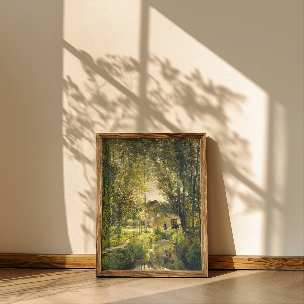 A framed landscape art print leaning against a beige wall on a wooden floor, showing a sunlit green forest scene with trees and a small building. The artwork is enclosed in a light natural wood frame, and strong window shadows are cast across the wall and floor.