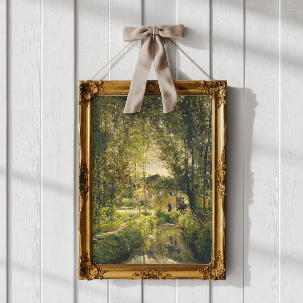 A framed landscape painting of a sunlit forest scene with trees, water, and a small house, displayed on a white paneled wall with a beige ribbon bow at the top.