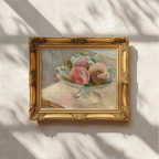 An ornate gold picture frame containing a still life painting of pink flowers, mounted on a textured off-white wall with soft window shadow patterns.