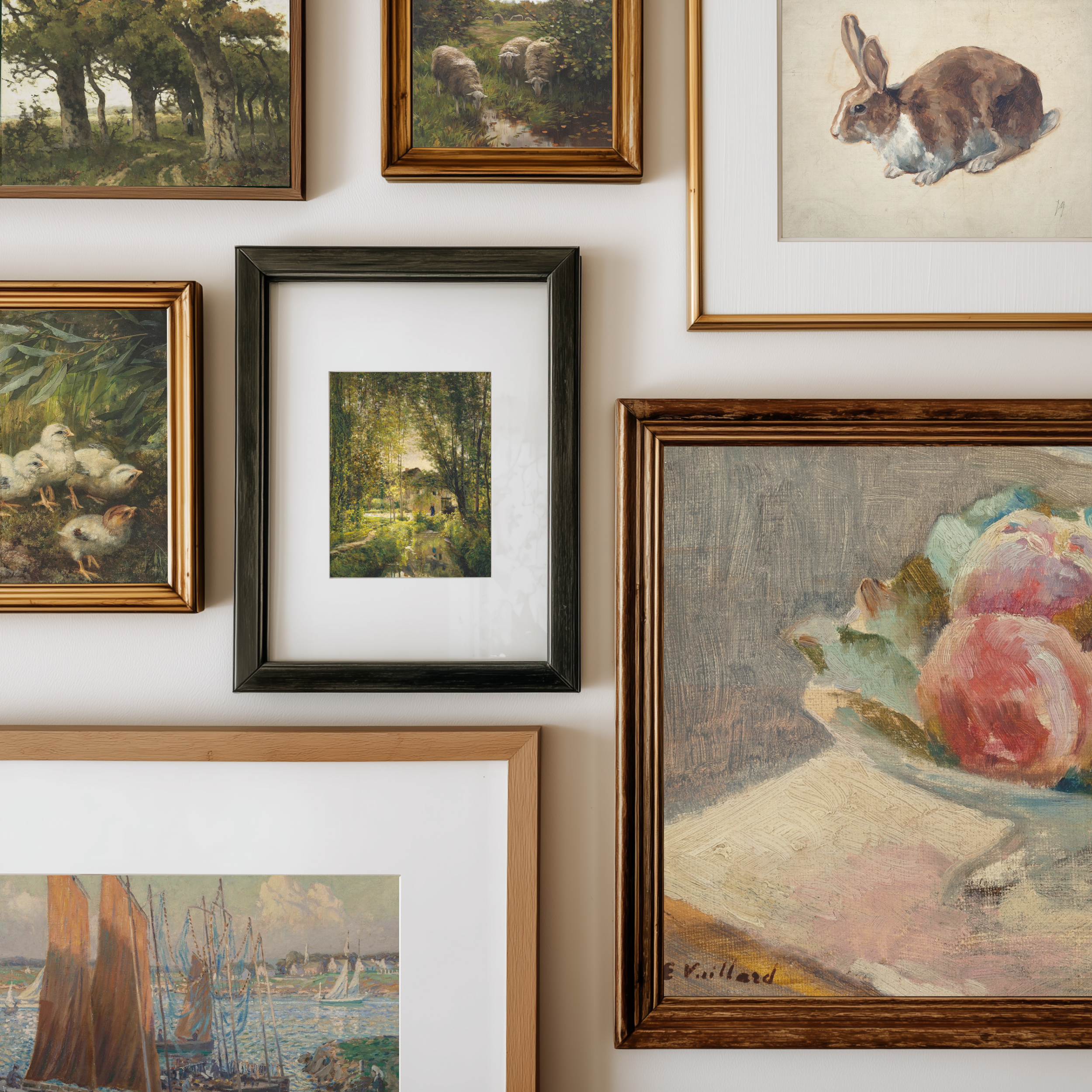 A gallery wall display of multiple framed art prints and paintings, including landscapes, still life fruit, a rabbit, ducks, and a harbor scene, arranged on a white wall.