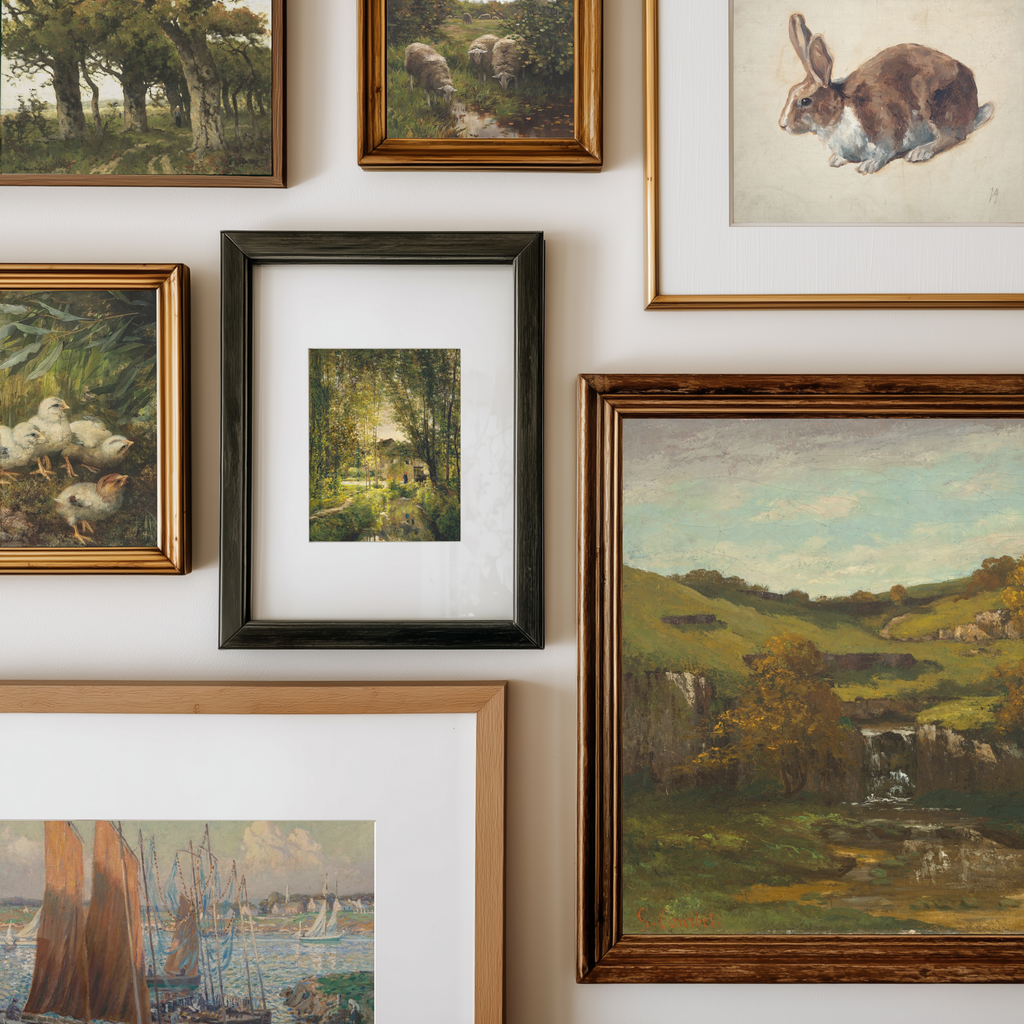 A gallery wall display of multiple framed art prints and paintings, including landscapes, a rabbit illustration, ducks, and a small central forest scene in a black frame.