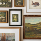 A gallery wall display of multiple framed art prints and paintings, including landscapes, a rabbit illustration, ducks, and a small central forest scene in a black frame.