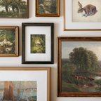 A gallery wall display of multiple framed art prints and paintings, including landscapes, a rabbit illustration, ducks, and cows by a river, arranged in a clean grid on a white wall.