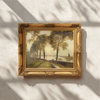 An ornate gold picture frame holding a landscape painting with tall trees and a pale sky, mounted on a textured off-white wall with soft window-shadow light casting across the scene.