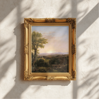 An ornate gold picture frame holding a landscape painting, mounted on a textured white wall with soft shadows cast across it.