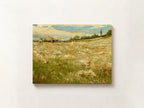 A horizontal canvas painting of a rural landscape, featuring a golden field under a cloudy blue sky, mounted on a light beige wall.